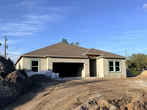 Single-story house under construction with open garage and dirt lot in front under a clear blue sky