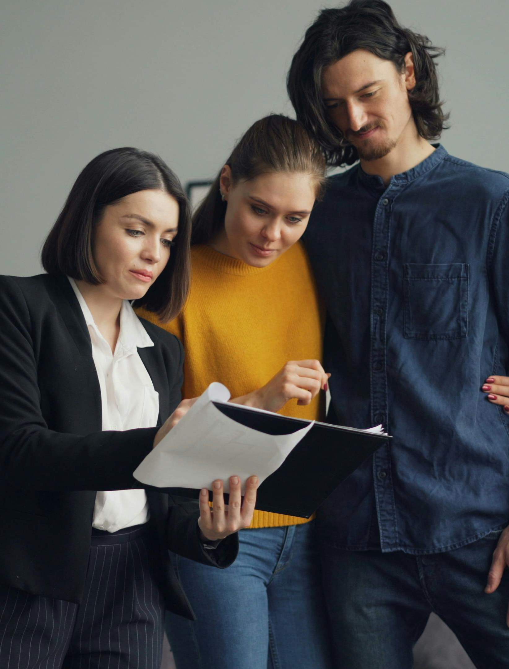 A woman in a black blazer explains documents to a couple, who are looking at the papers with focused expressions.