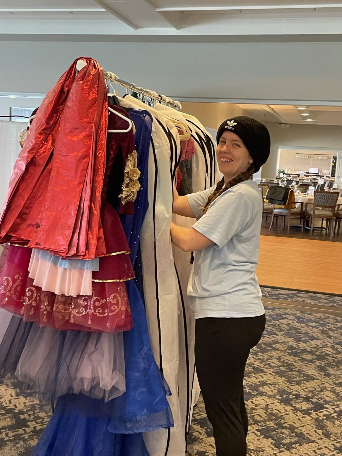 Person sorting colorful dresses on a clothing rack in a store, smiling indoors