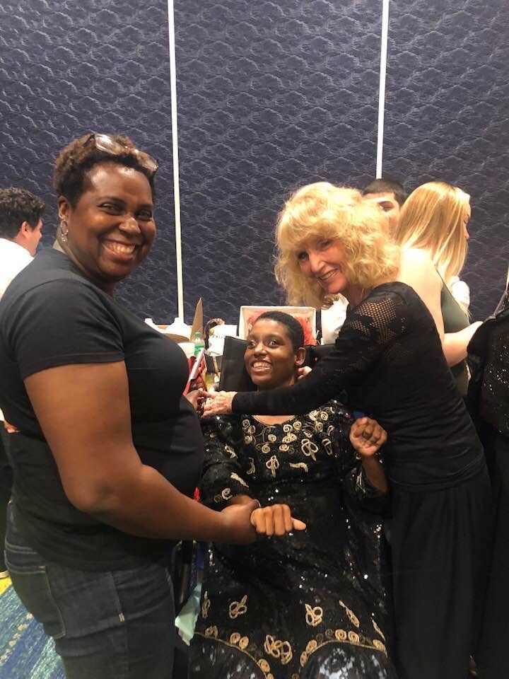 Three people smiling around a seated person in a wheelchair at an indoor event