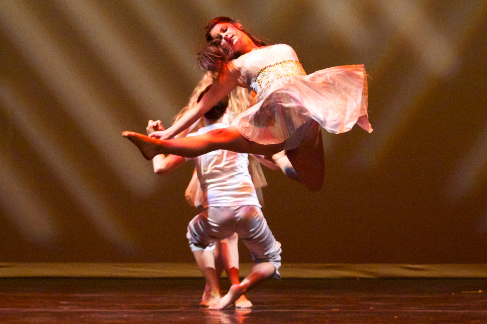 Two dancers performing a lift on stage. One dancer is upside down, lifting the other in a flowing white dress.