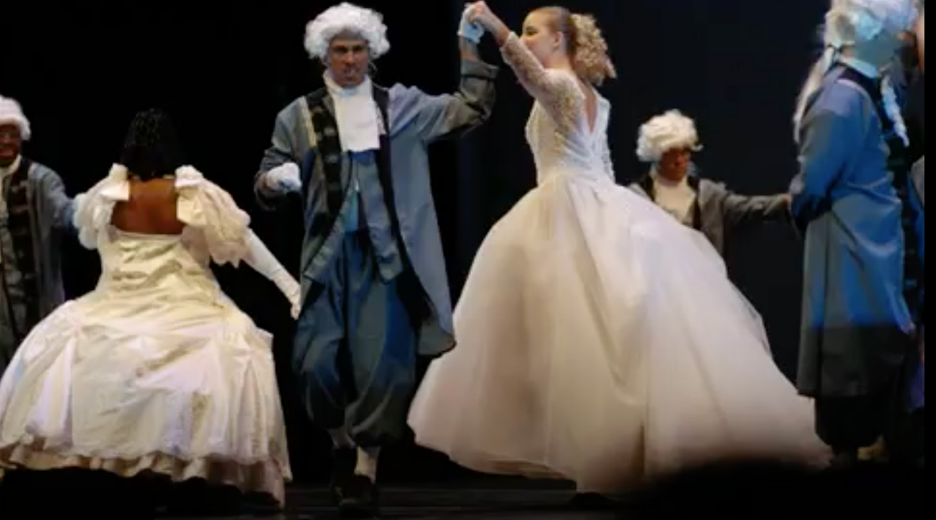 Actors in powdered wigs and period costumes dancing on stage.
