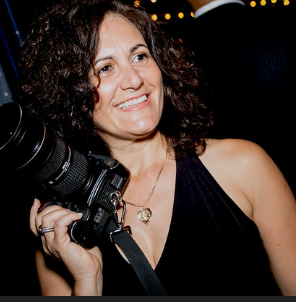 Woman smiling while holding a camera at a dimly lit event