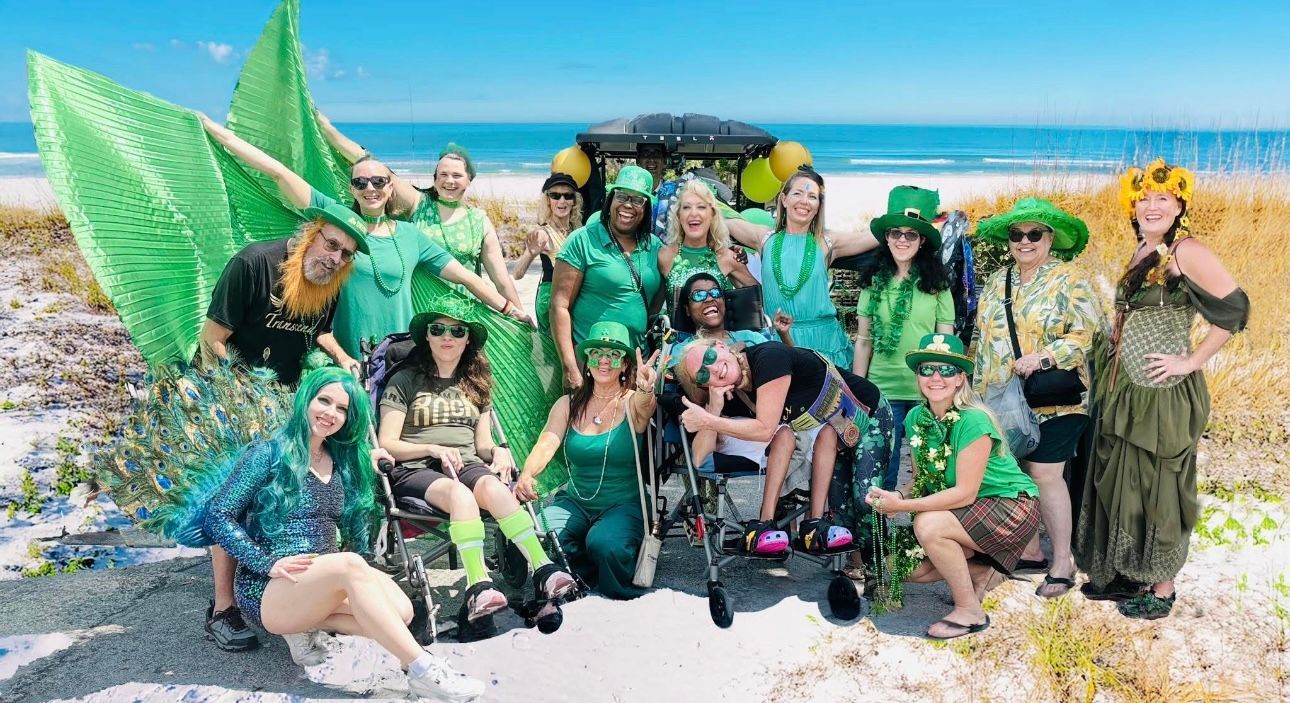 Group of people posing on a tropical beach with green costumes and beach props