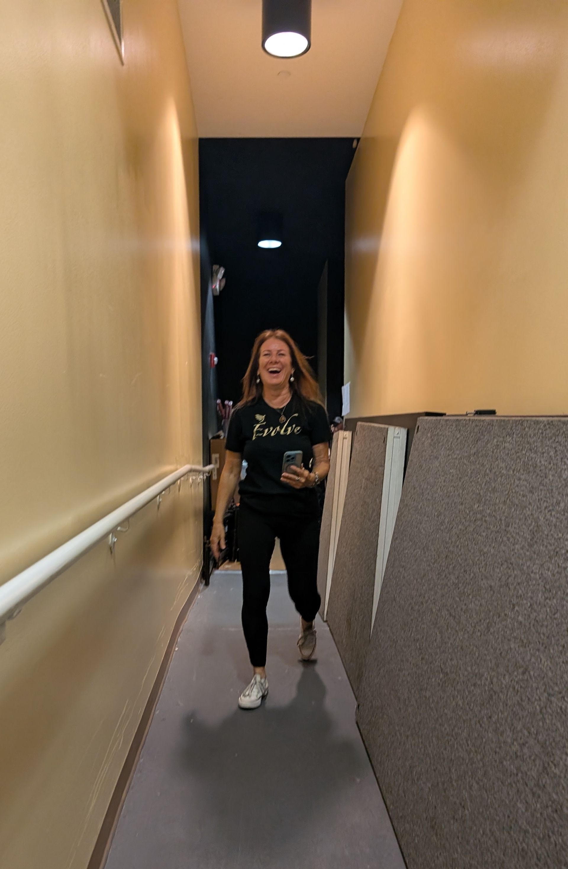 Person standing in a narrow hallway with yellow walls and gray carpet, facing the camera.