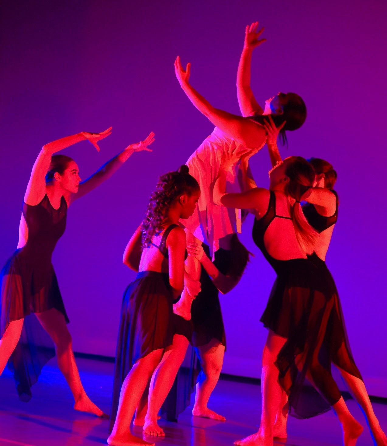 Dancers in black and white outfits performing on stage under red and blue stage lighting.