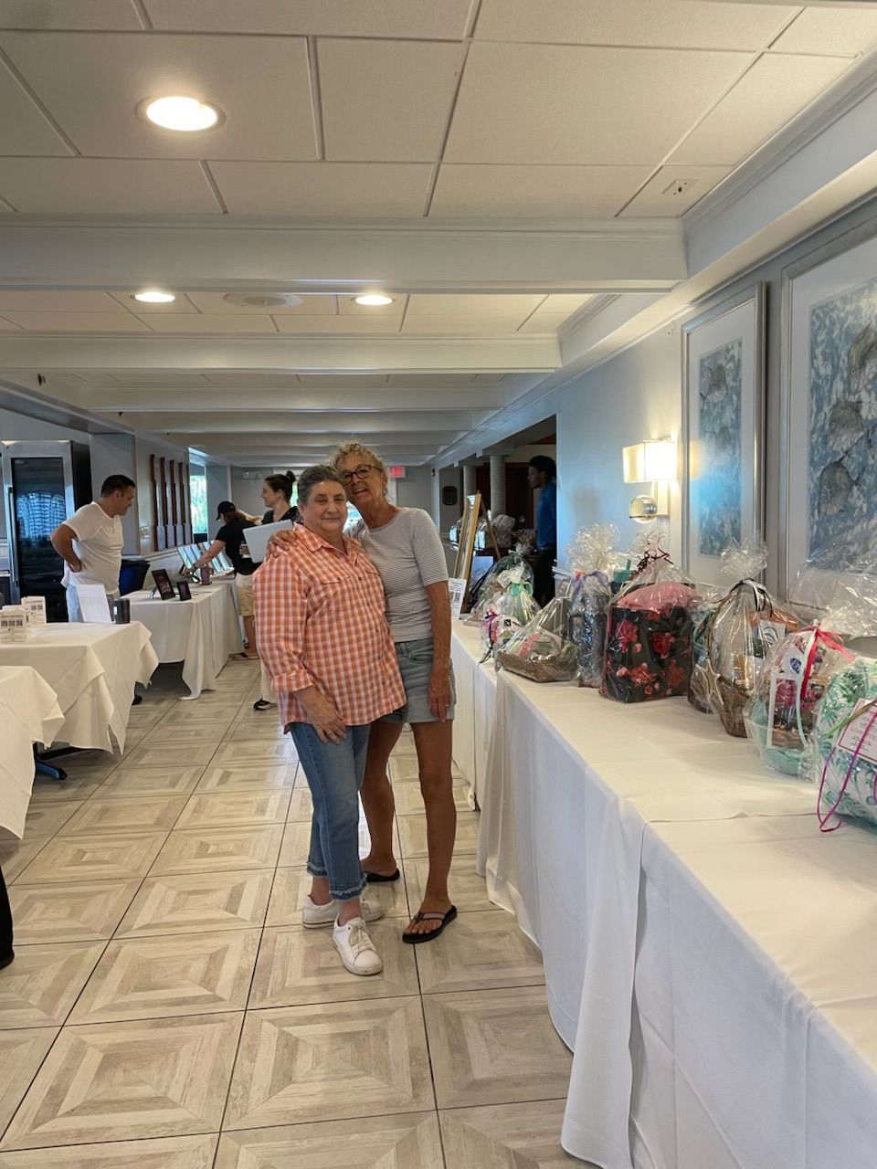 Two people standing in a decorated indoor banquet hall with gift baskets on tables