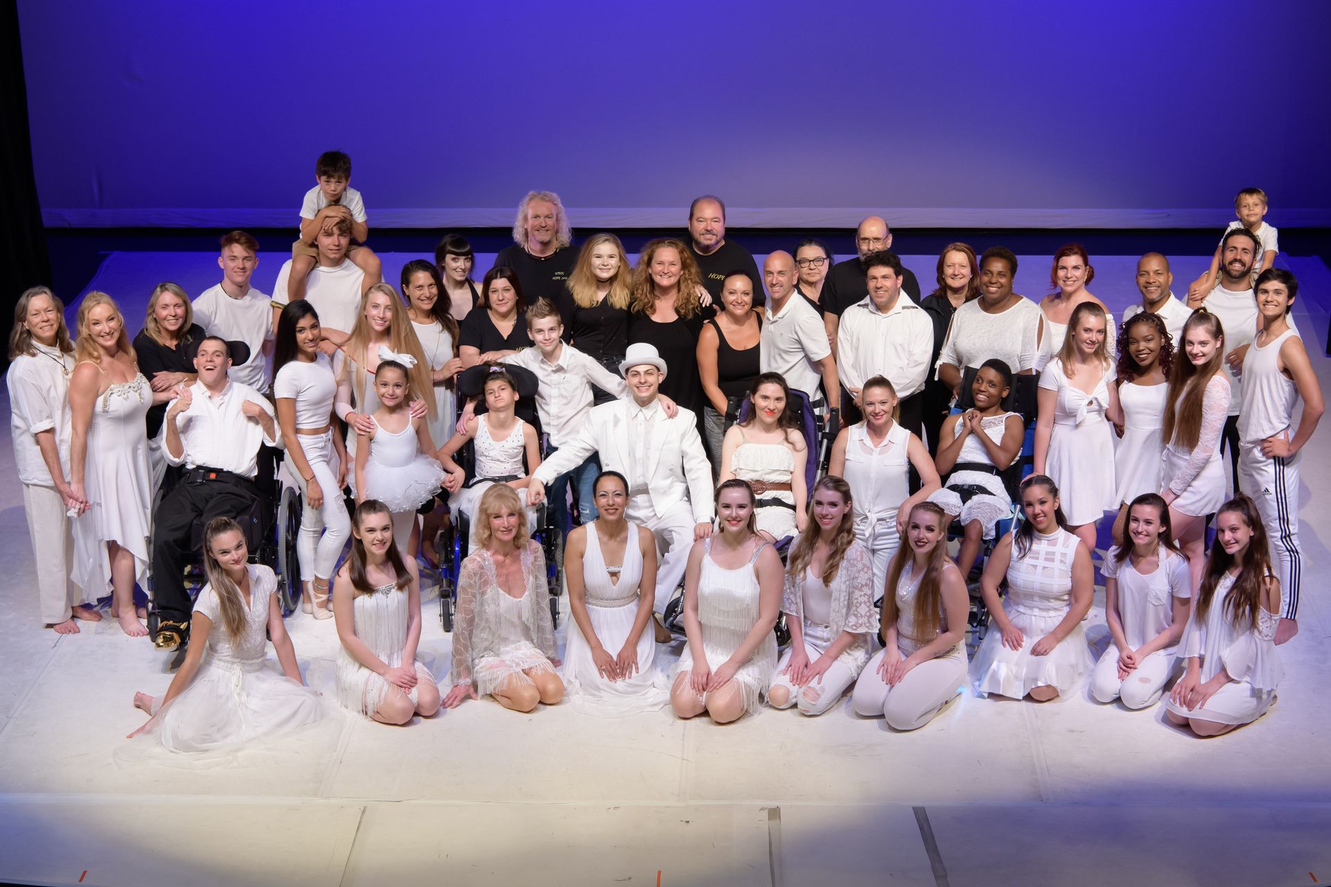 Group of people in white clothing on a stage with a blue backdrop.