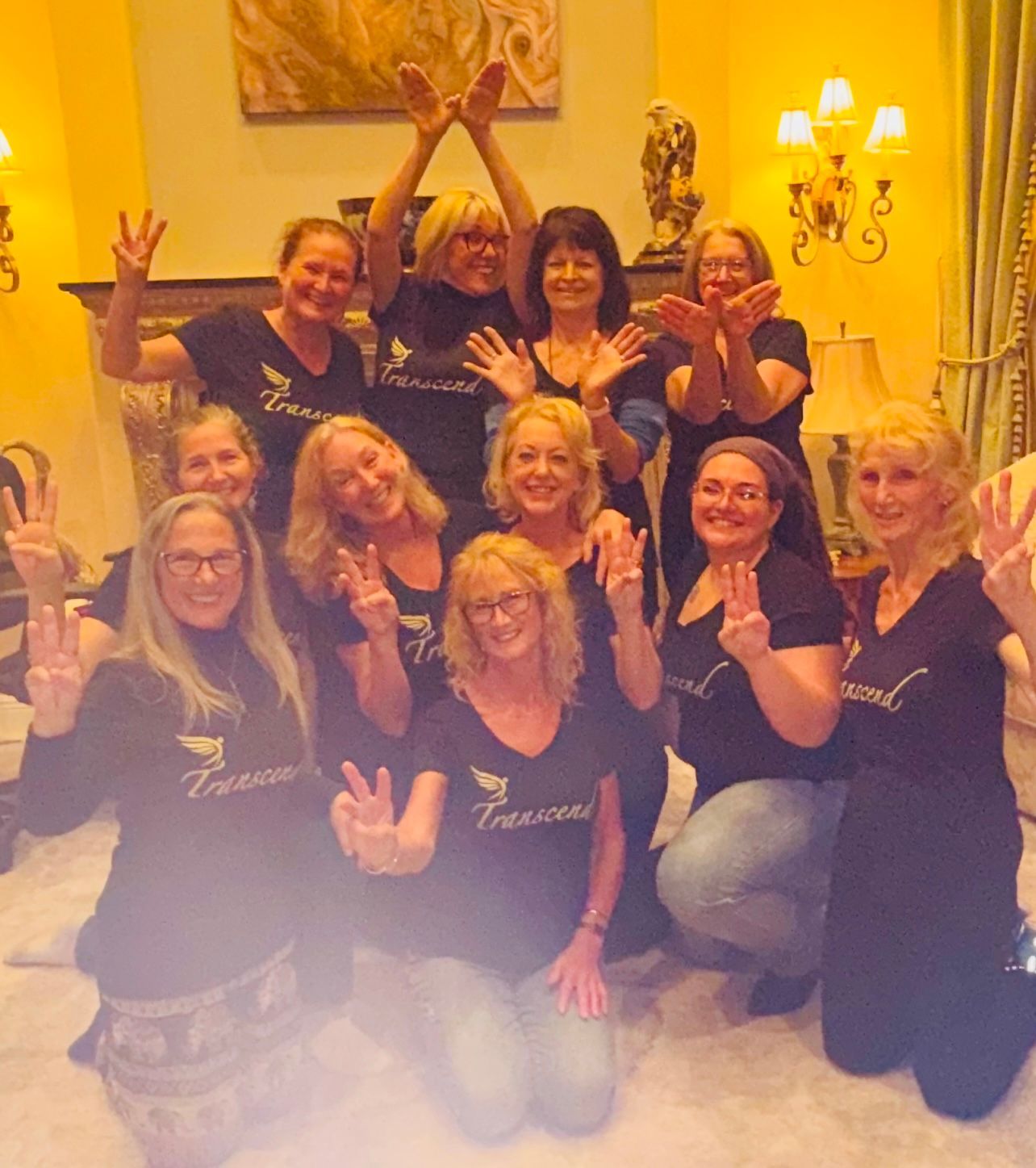 Group of smiling women posing indoors, wearing matching black shirts and making playful hand gestures.