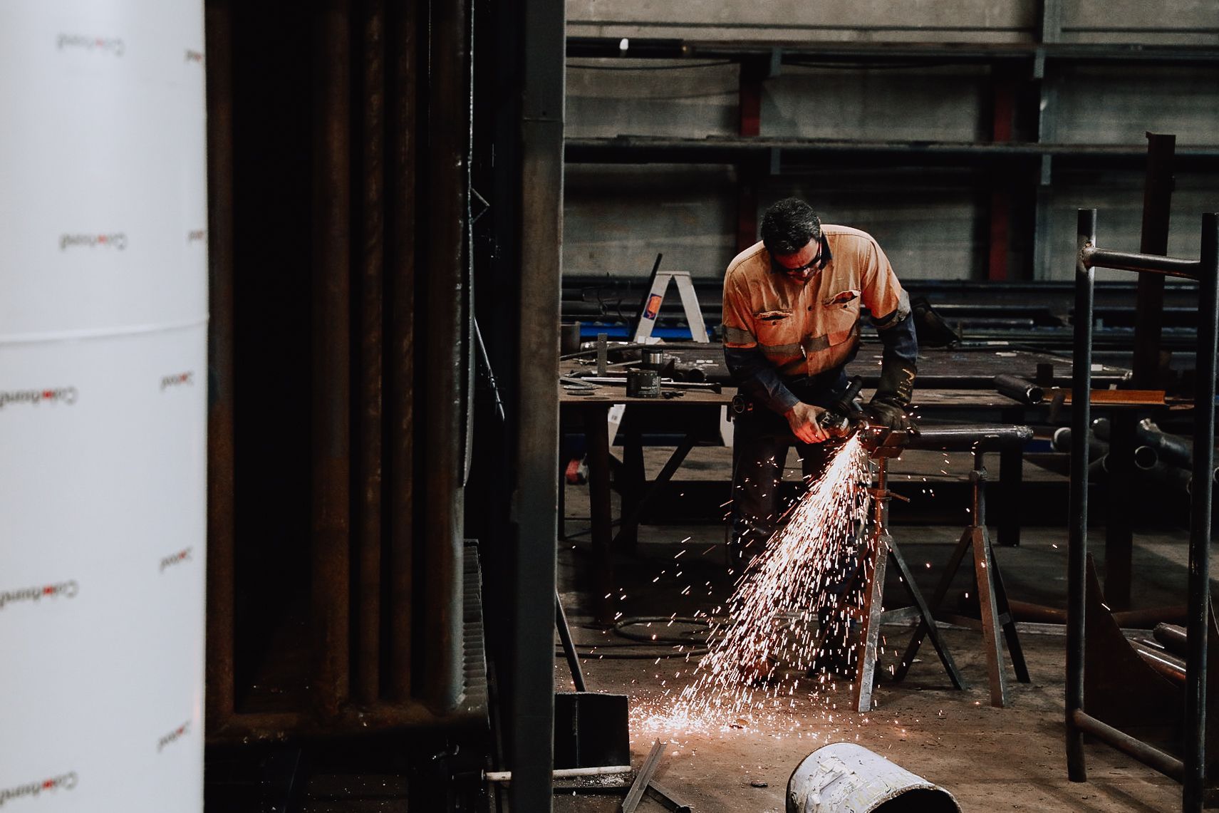 A worker uses a power tool to grind metal in a workshop, creating a cascade of bright sparks.