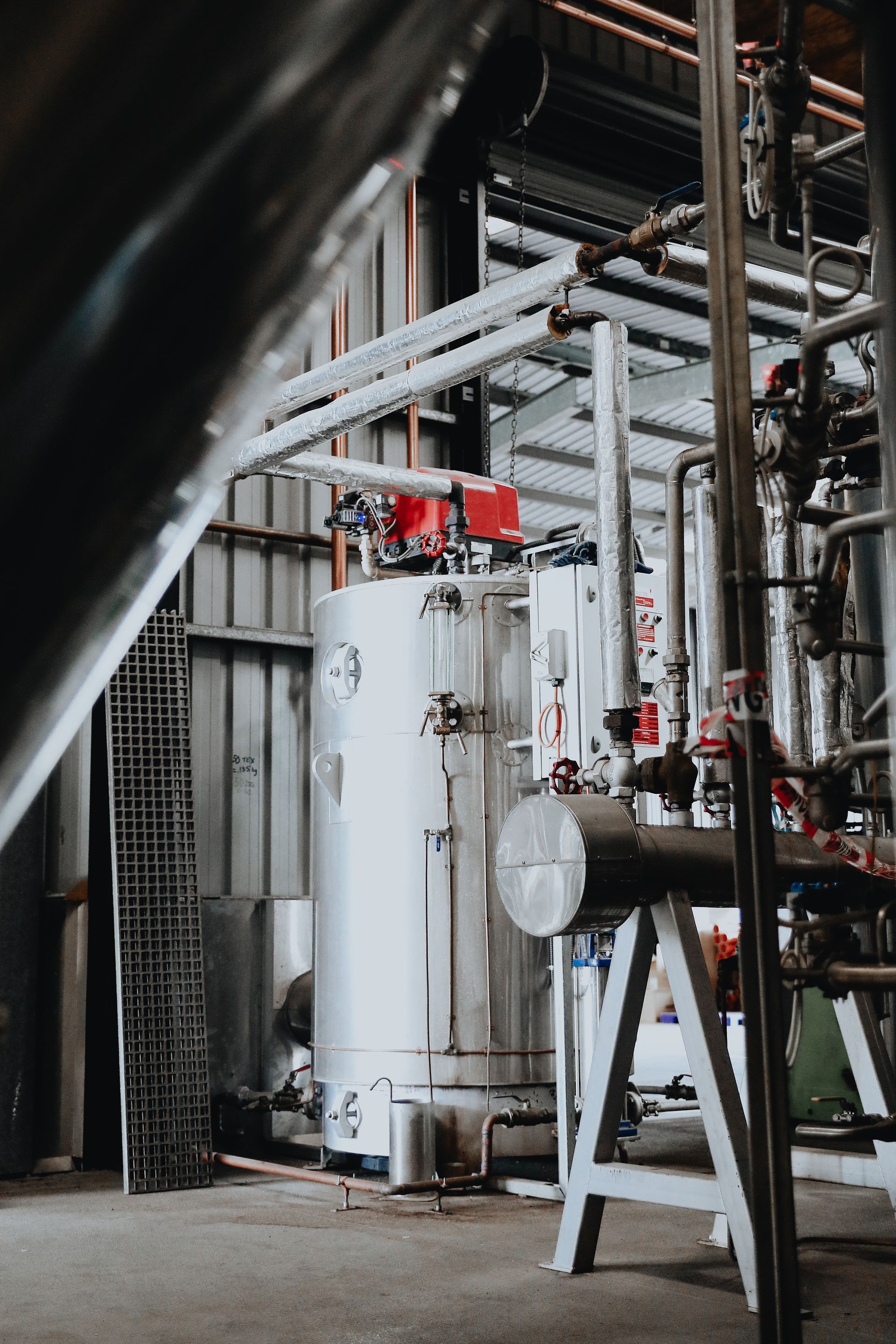 Industrial facility interior featuring a large metallic cylindrical tank, complex piping, and metal structural supports.