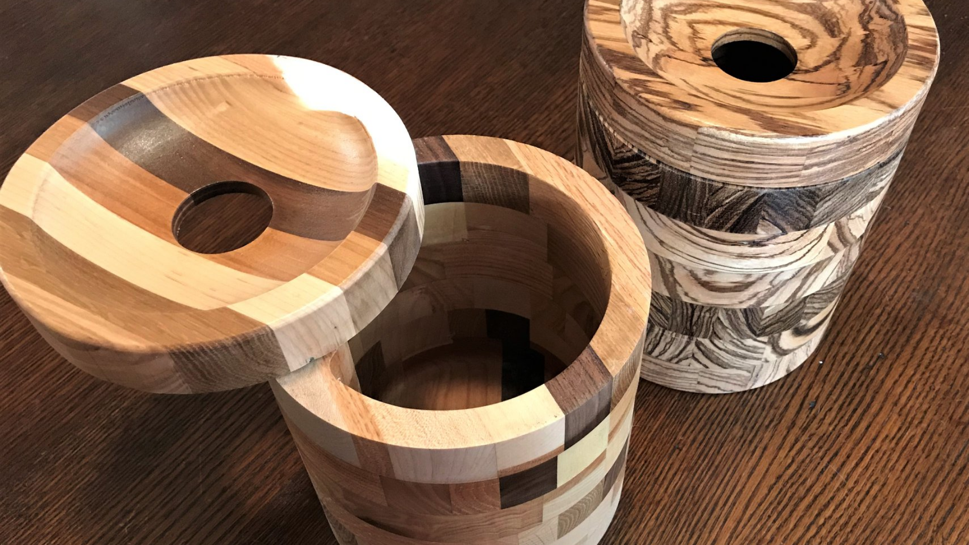 Two handcrafted wooden canisters with circular, cutout lids sitting on a dark wooden surface.