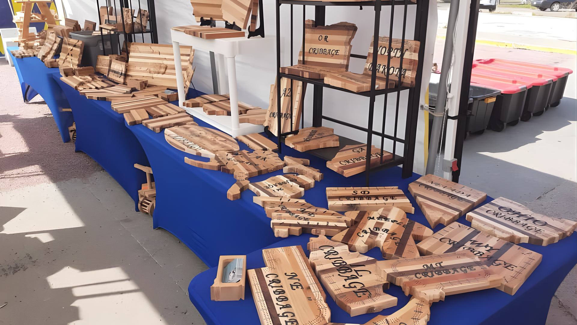 A market stall displays various handmade wooden items, including engraved signs and boards, arranged on a blue-covered table.