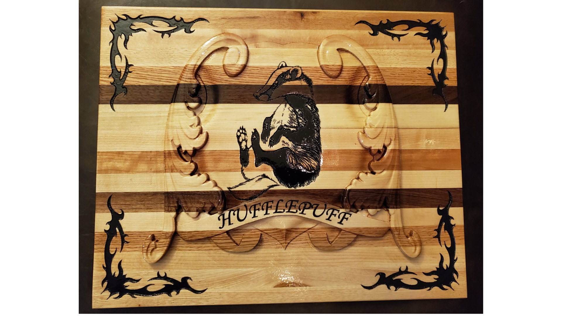 A wooden cutting board with a carved Hufflepuff badger crest, decorative flourishes, and scrollwork accents.