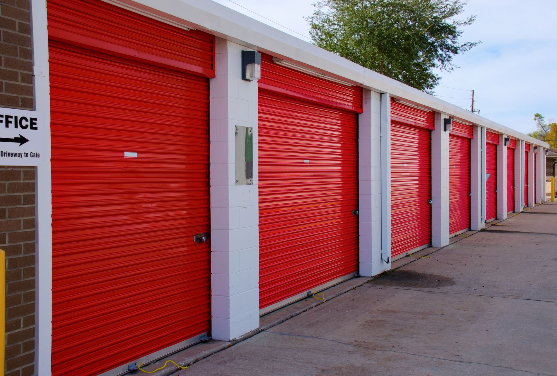 Row of blue roll-up doors at a self-storage facility under a partly cloudy sky Rental storage units.