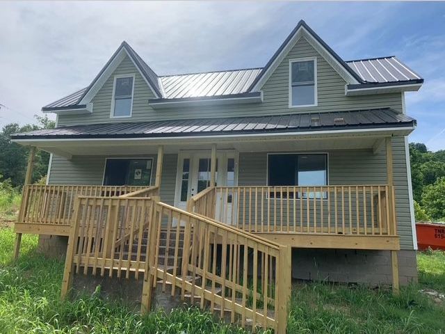Two-story gray house with front porch and wooden ramp under a partly cloudy sky