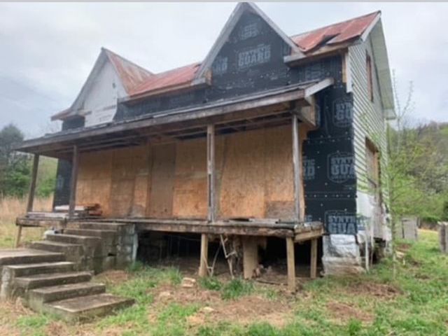 Abandoned boarded-up house with a porch and worn steps in a grassy, overgrown yard