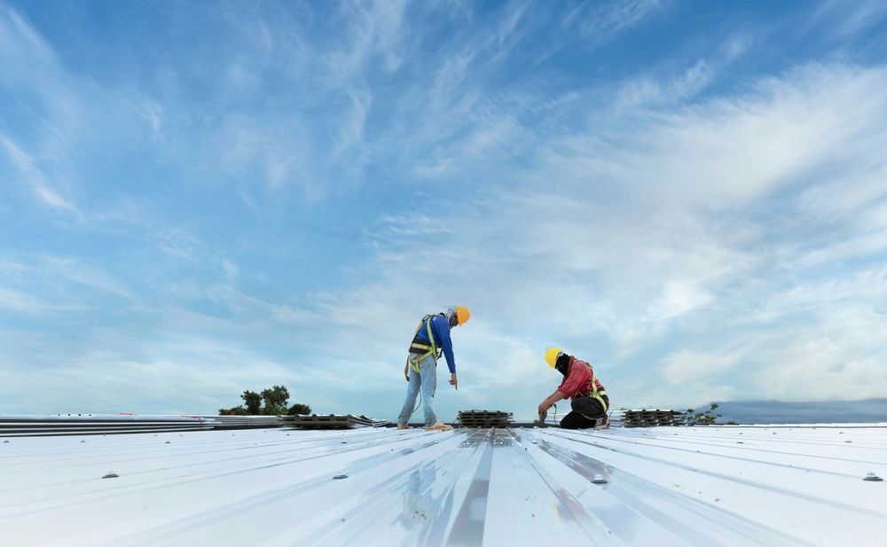 Two construction workers are working on a white roof.