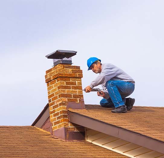 A man is working on a chimney on the roof of a house.