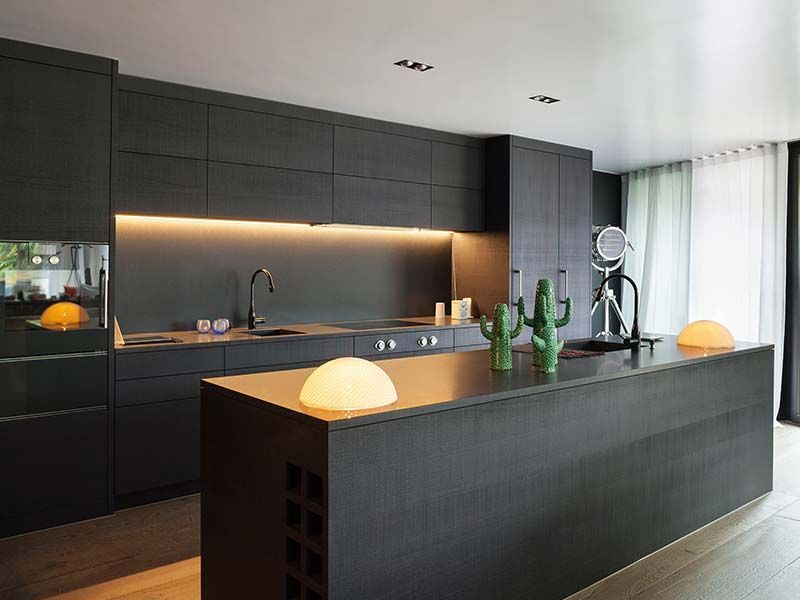 A kitchen with black cabinets and a large island in the middle.