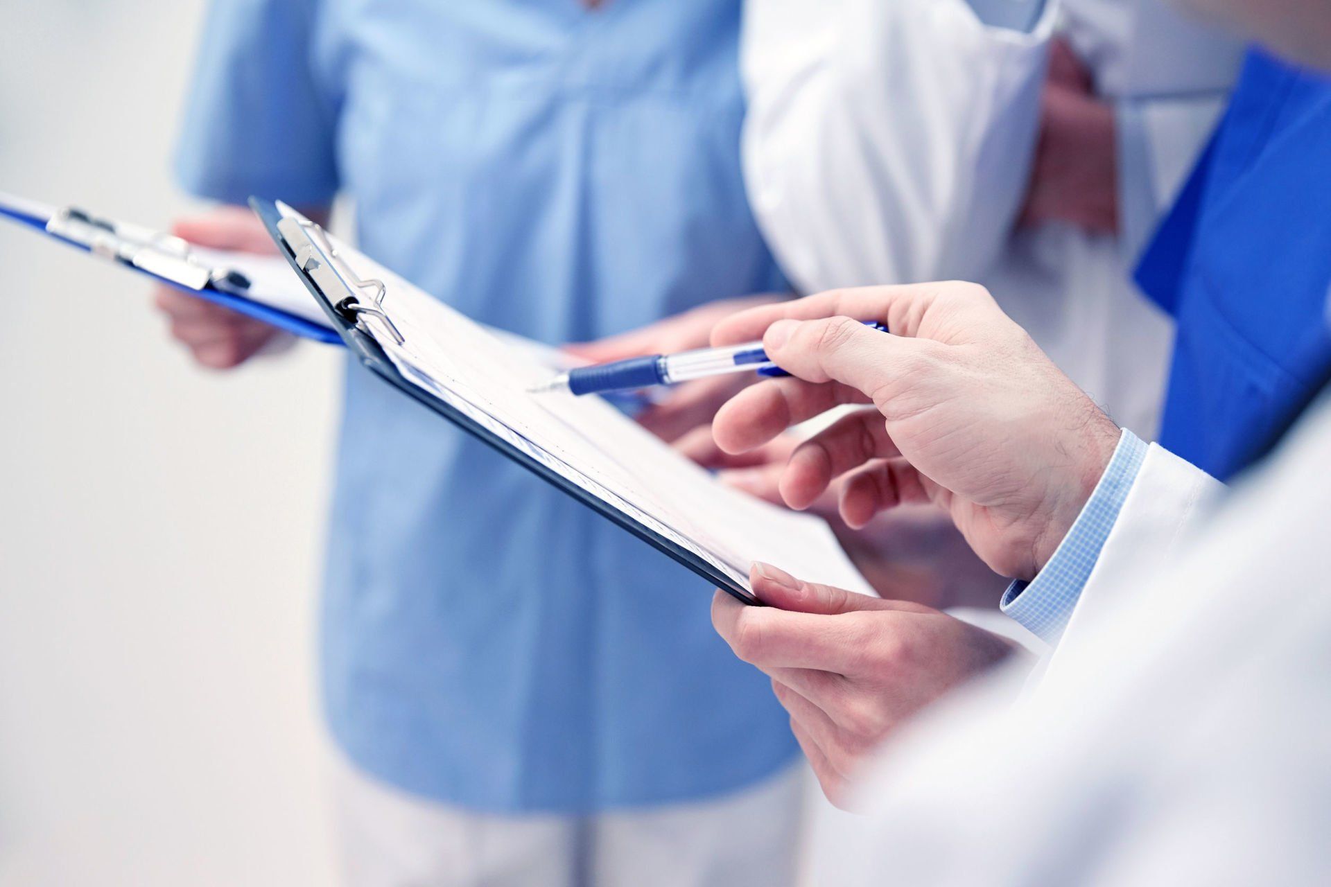 Medical providers in scrubs reviewing patient charts on a clipboard.