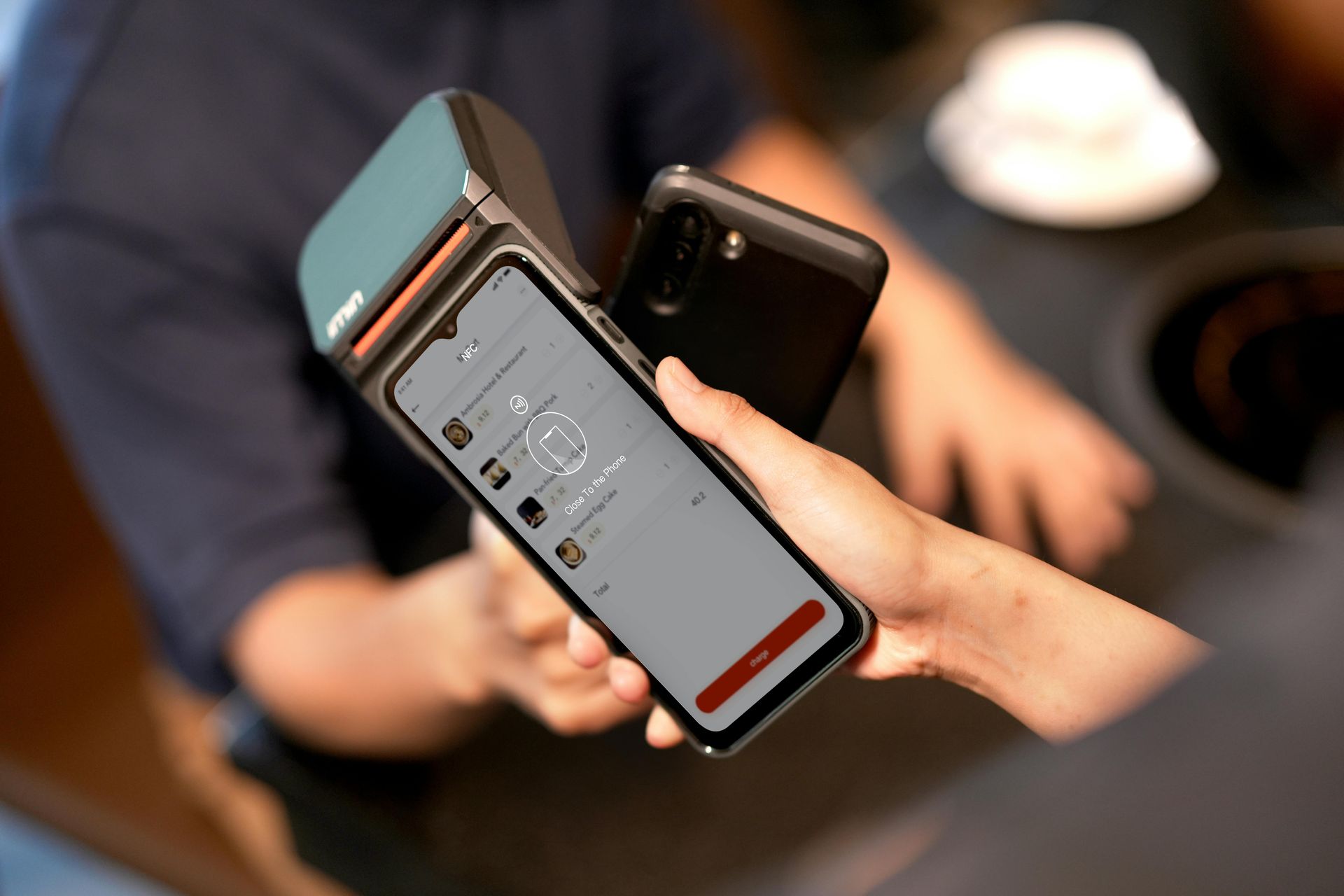Person using a smartphone to make a payment at a point-of-sale terminal; the screen shows payment options.
