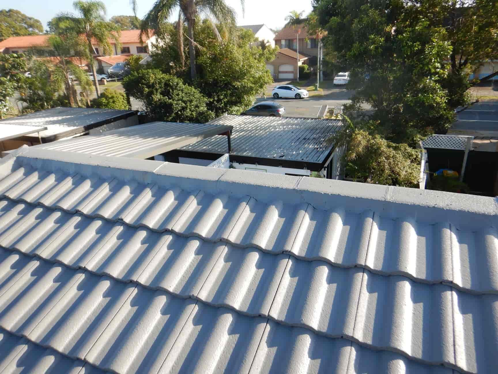 A Man Is Kneeling On A Roof Holding A Piece Of Paper — Gold Coast Roof Repairs in Ormeau, QLD