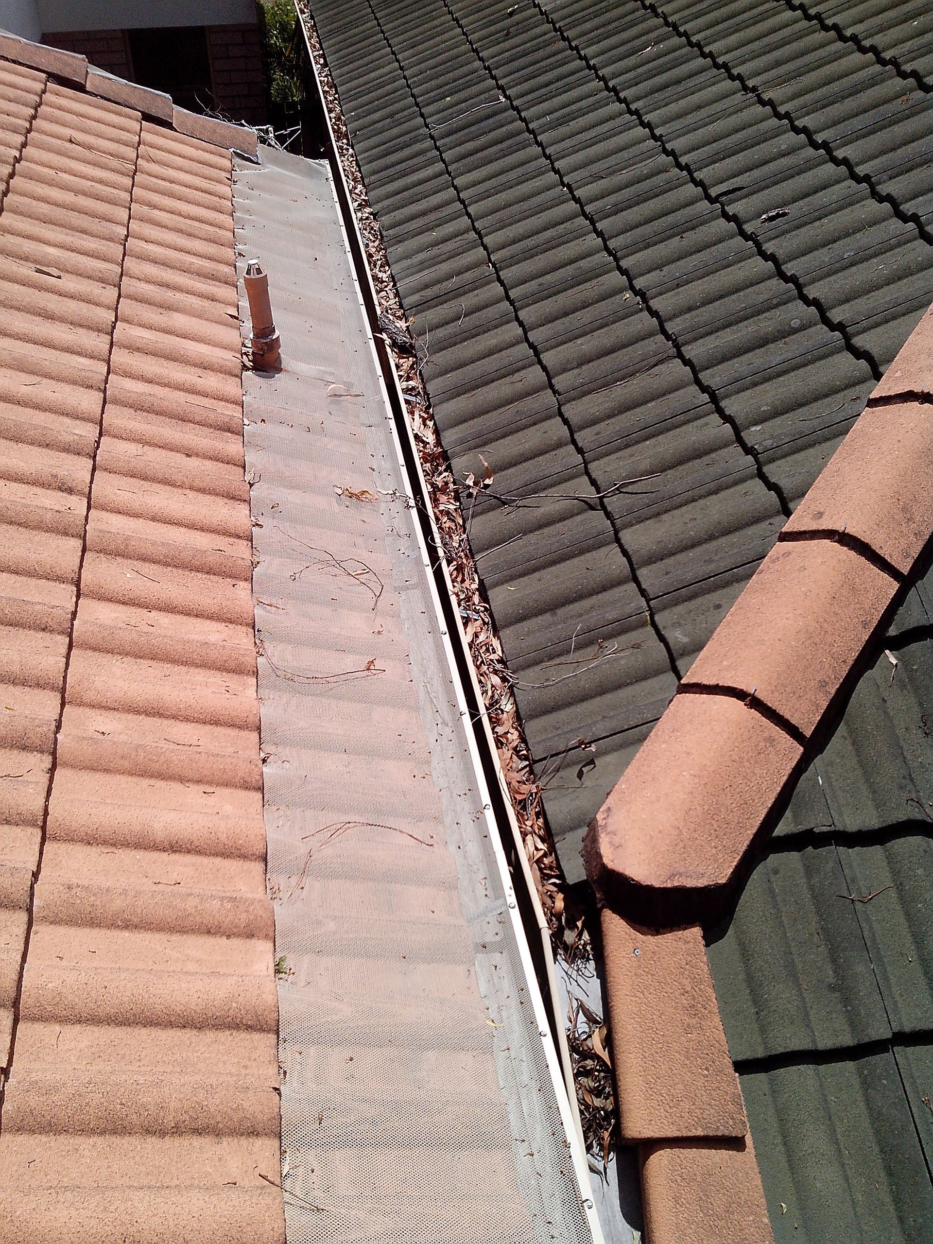 A Man Is Working On The Roof Of A House — Gold Coast Roof Repairs in Oxenford, QLD