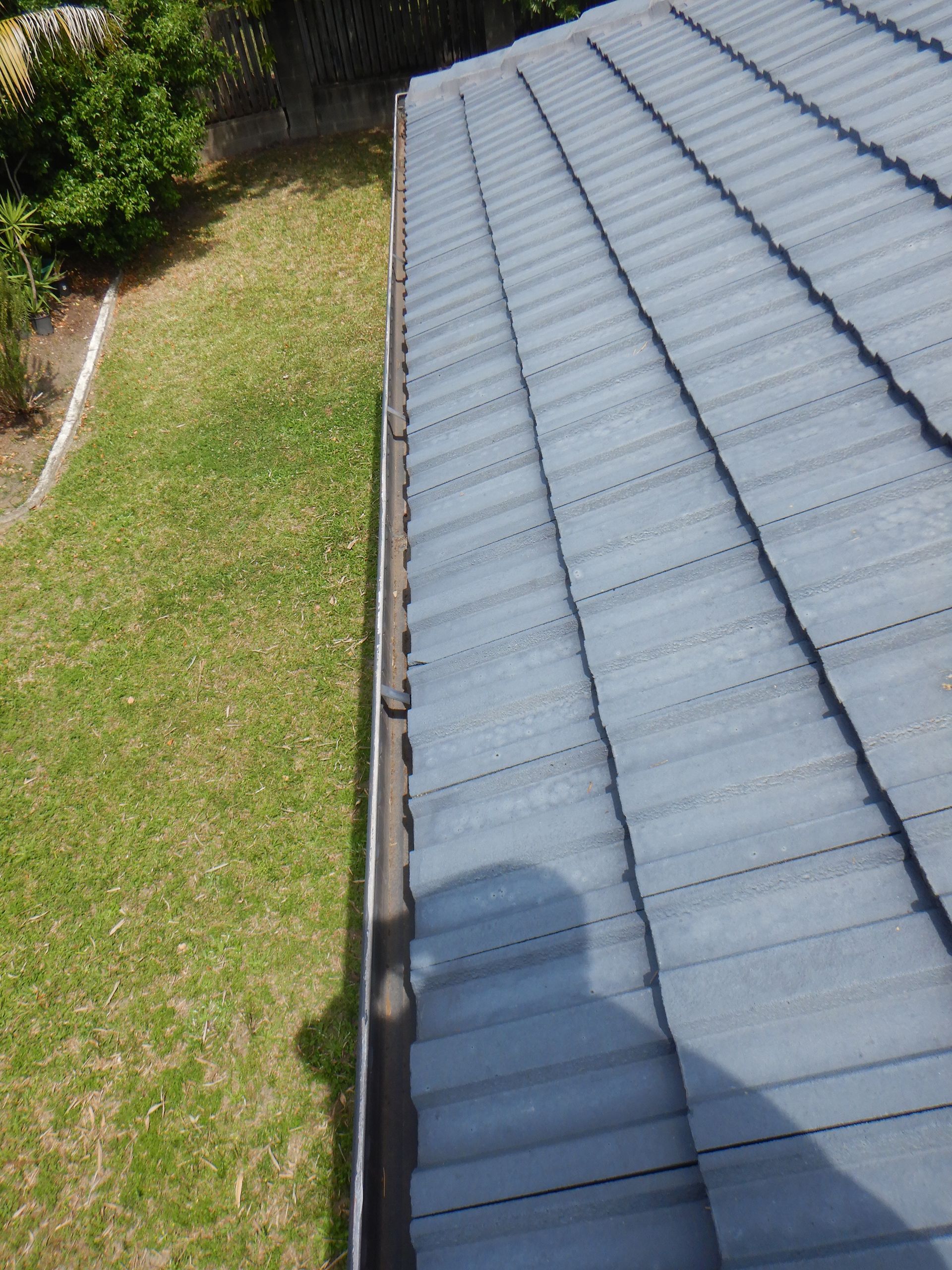 A Man Is Cleaning A Tiled Roof With A High Pressure Washer — Gold Coast Roof Repairs in Palm Beach, QLD
