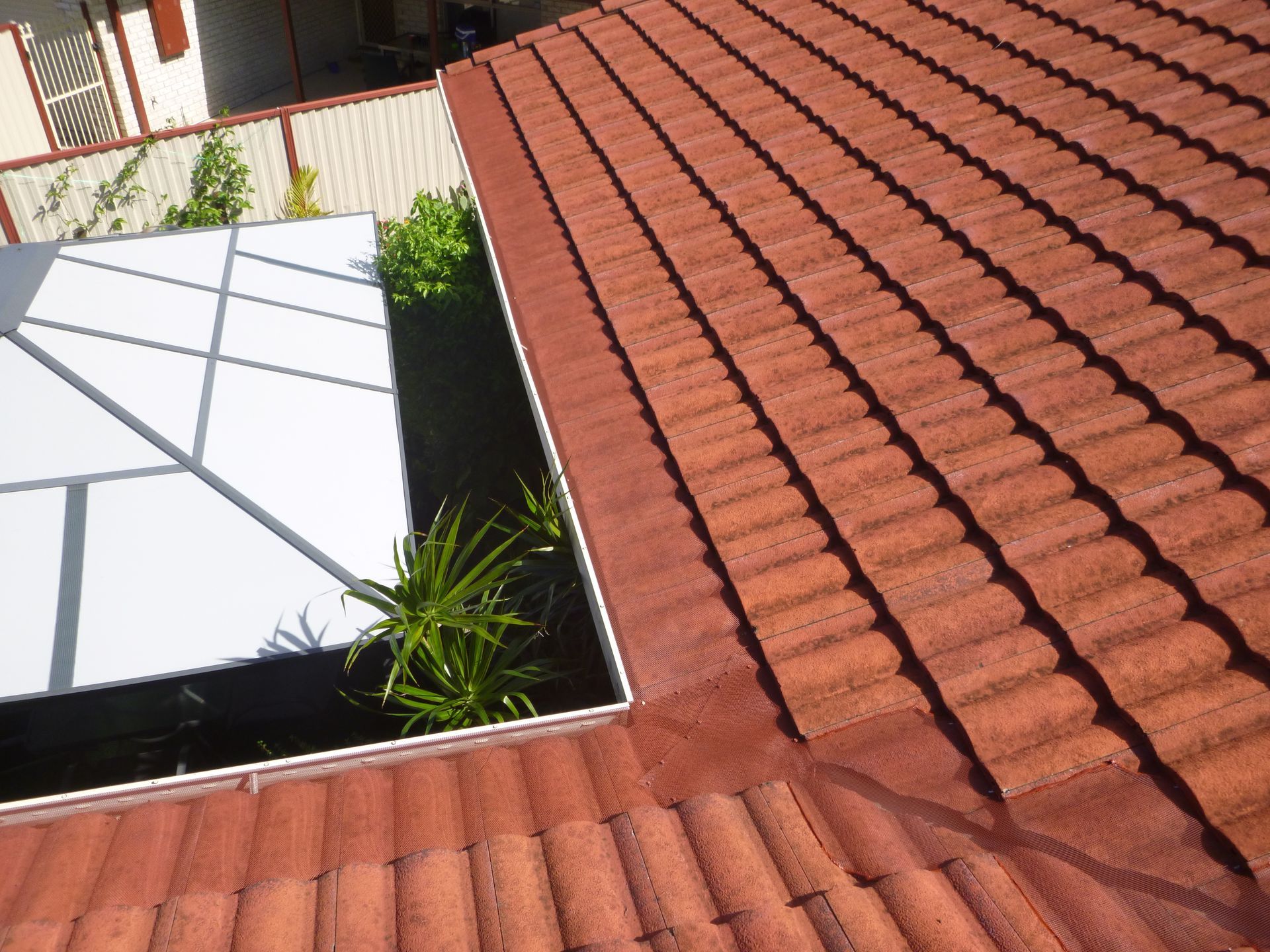 A Man Is Working On A Roof With A Brick Chimney — Gold Coast Roof Repairs in Ormeau, QLD