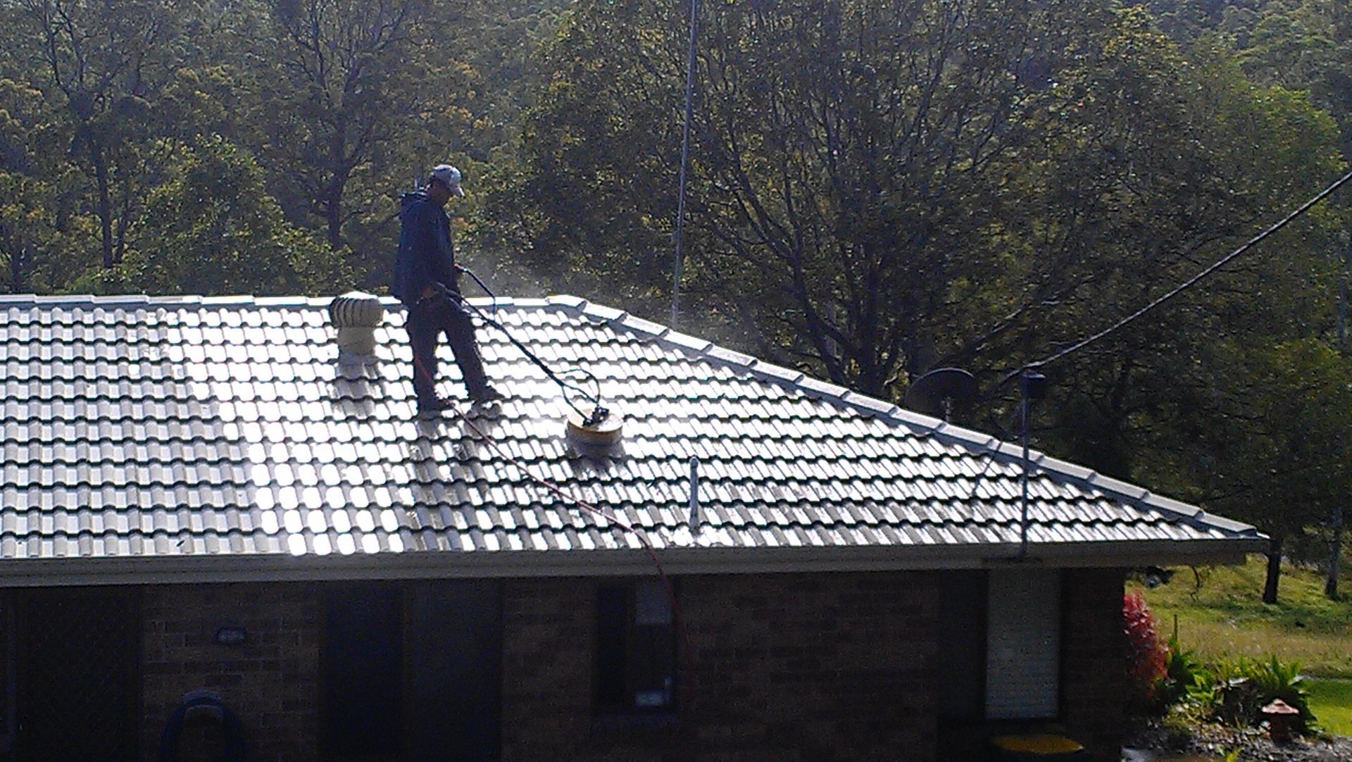 A Man Is Cleaning The Roof Of A House With A High Pressure Washer — Gold Coast Roof Repairs in Mudgeeraba, QLD