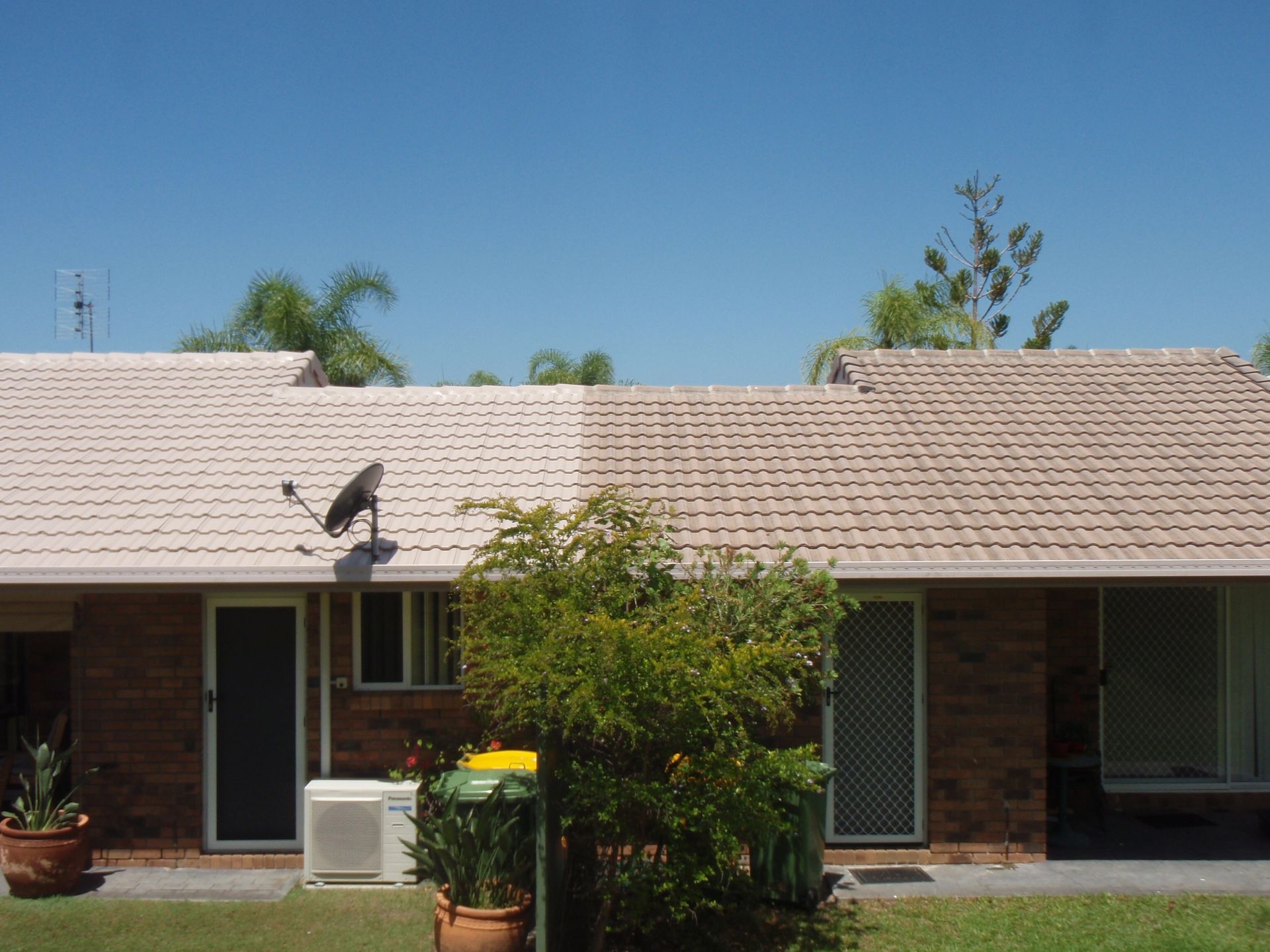 A Man Is Cleaning The Roof Of A House With A High Pressure Washer — Gold Coast Roof Repairs in Ormeau, QLD