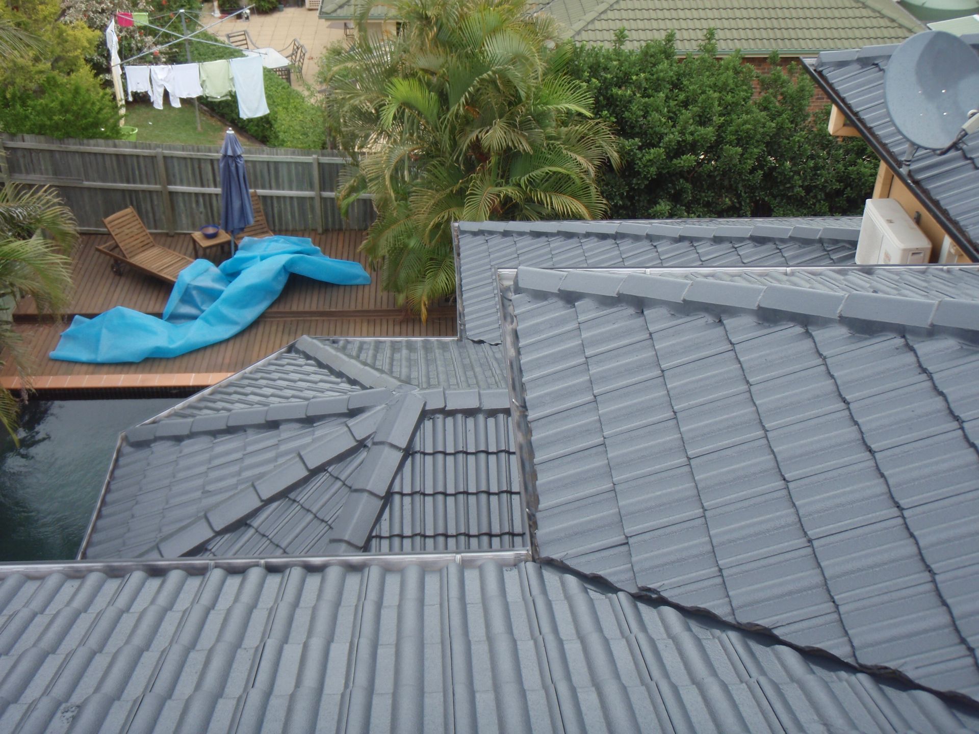 A Man Is Standing On Top Of A Tiled Roof — Gold Coast Roof Repairs in Southport, QLD