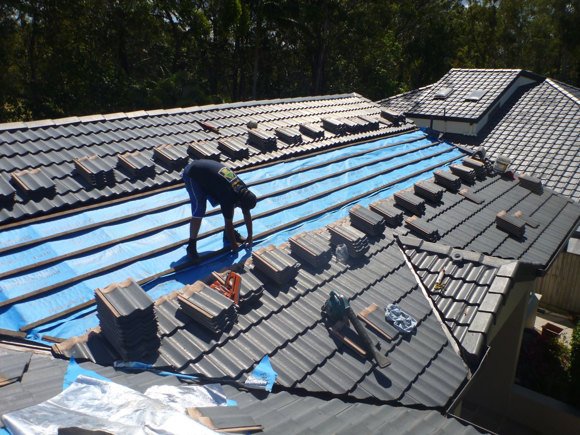 A Man Is Installing Tiles On A Roof — Gold Coast Roof Repairs in Oxenford, QLD