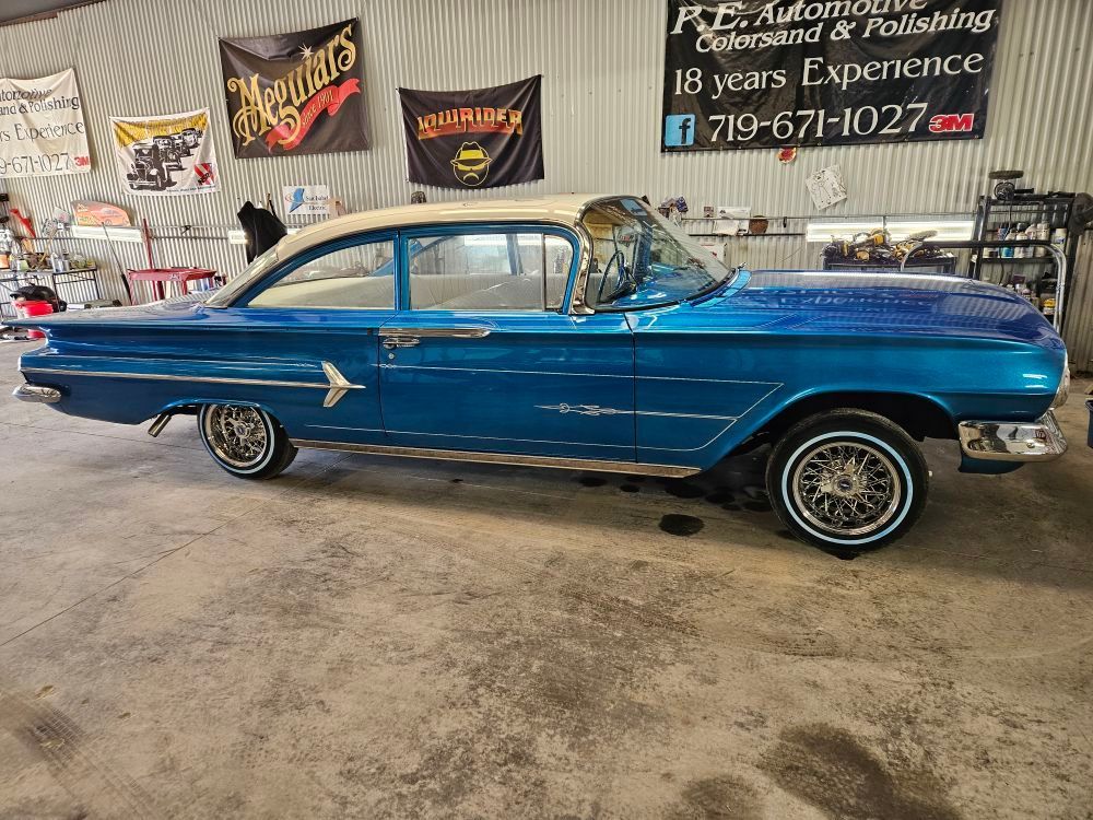 Blue vintage car with white roof and wire wheels in a shop.