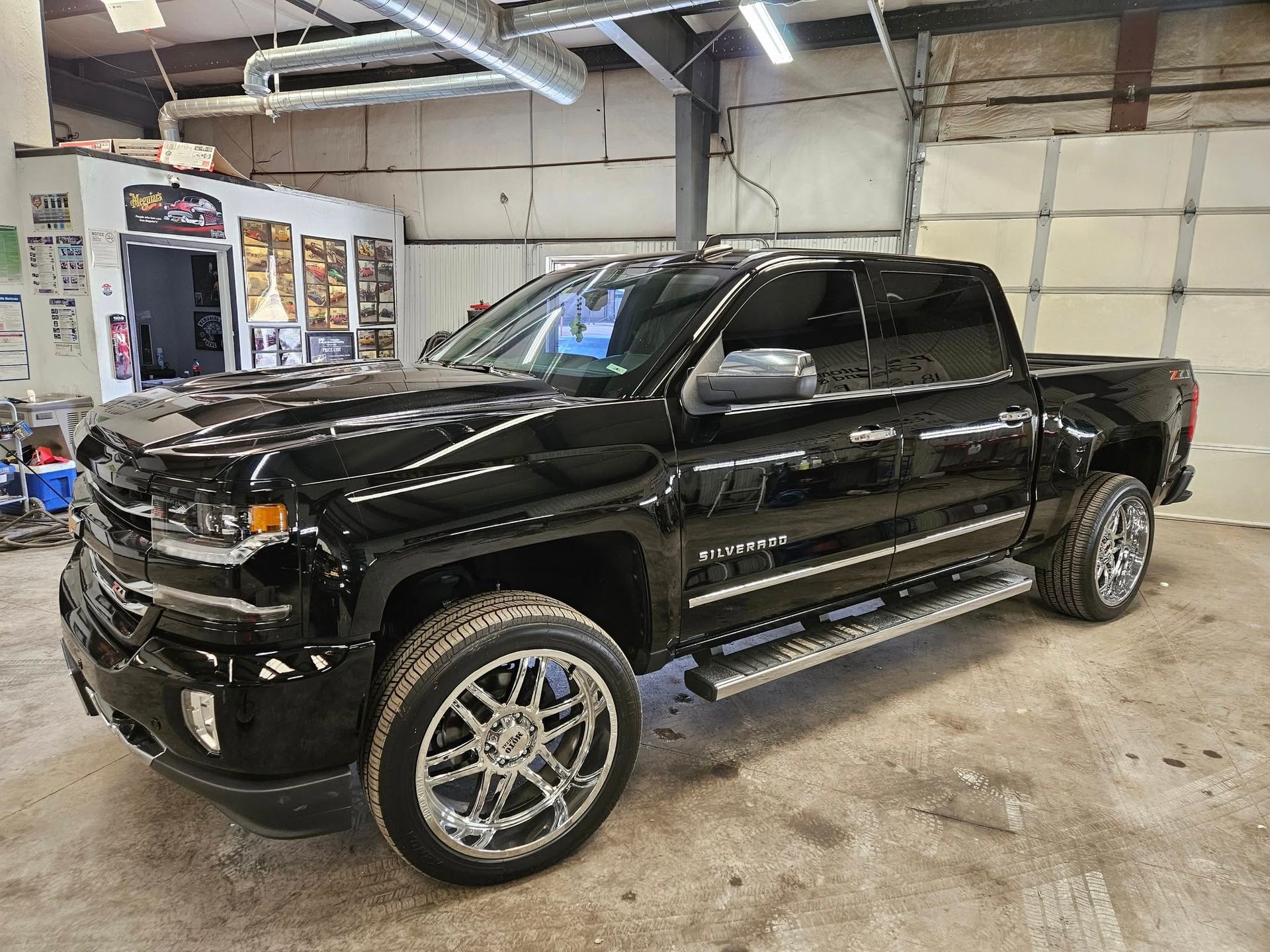 Black Chevrolet Silverado pickup truck with chrome wheels inside a garage.