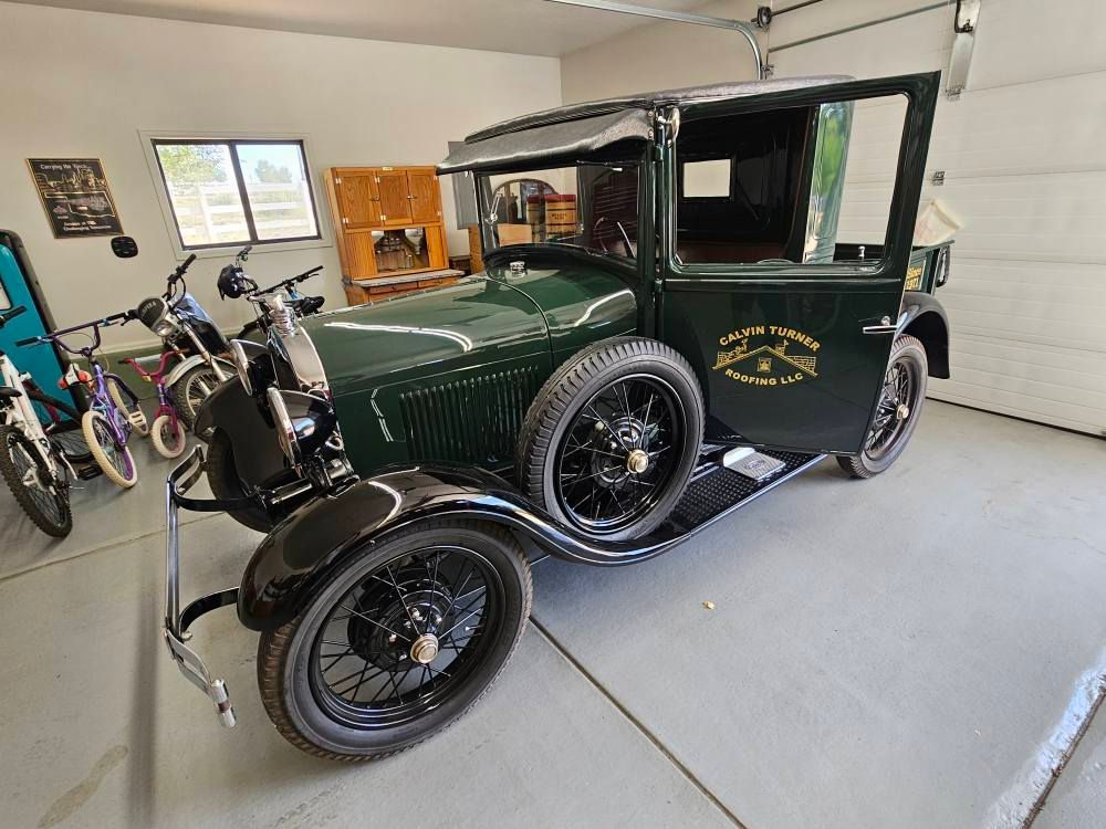 Green vintage car in a garage with open door; black wheels.