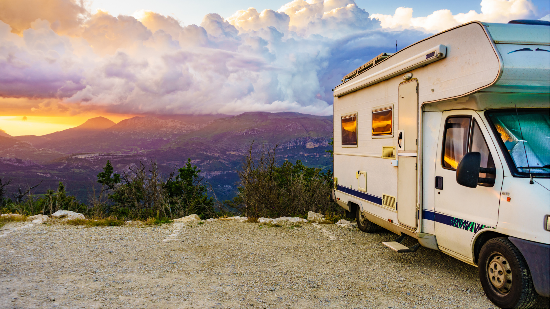 Camper van parked on a mountain overlook at sunset with clouds over a distant valley