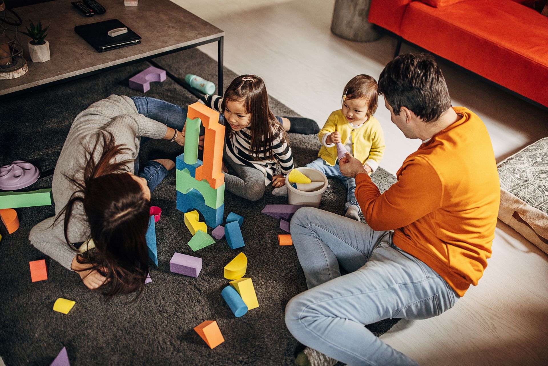 A family is playing with blocks on the floor in a living room.