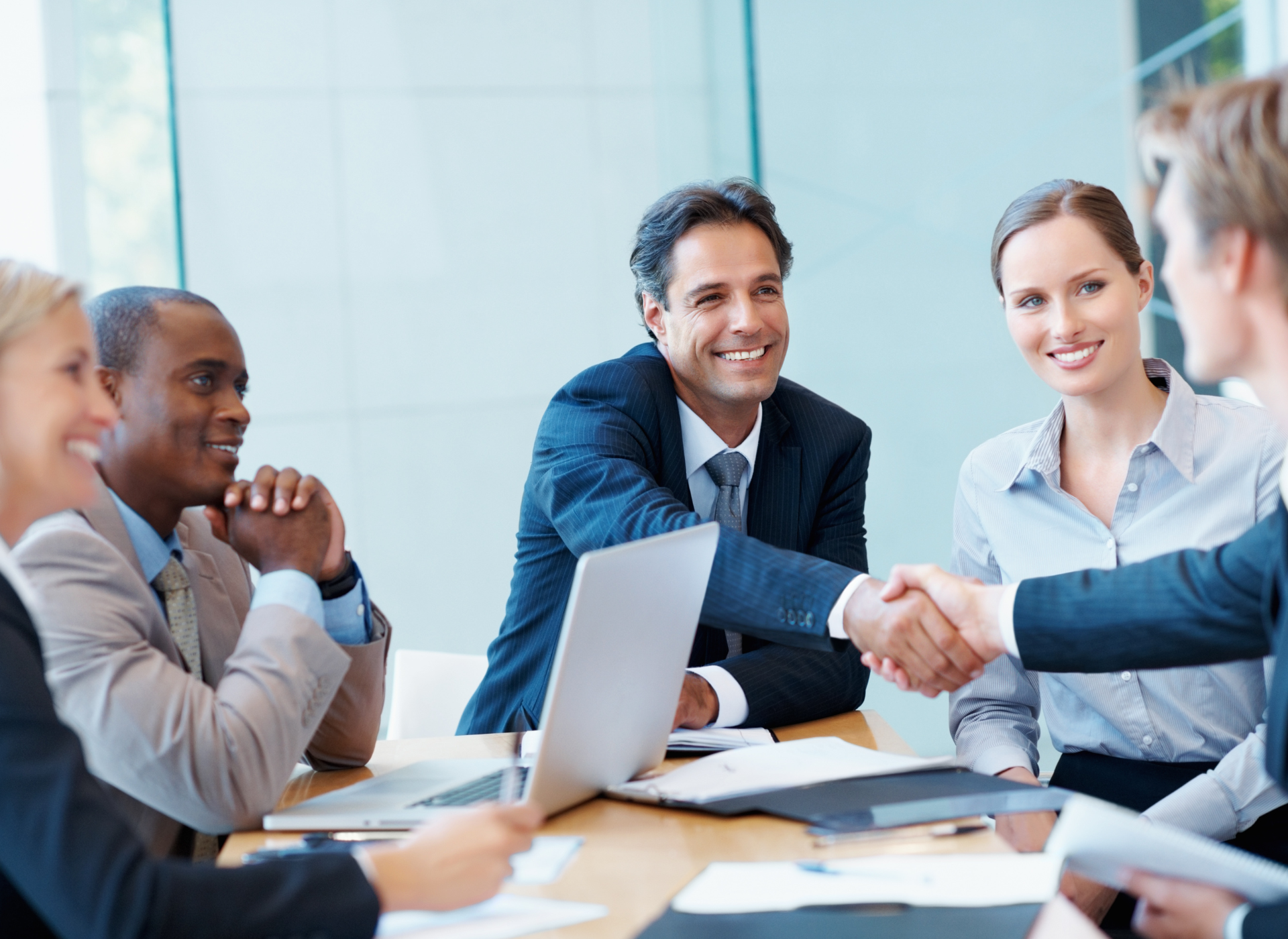 A group of business people are sitting around a table shaking hands.