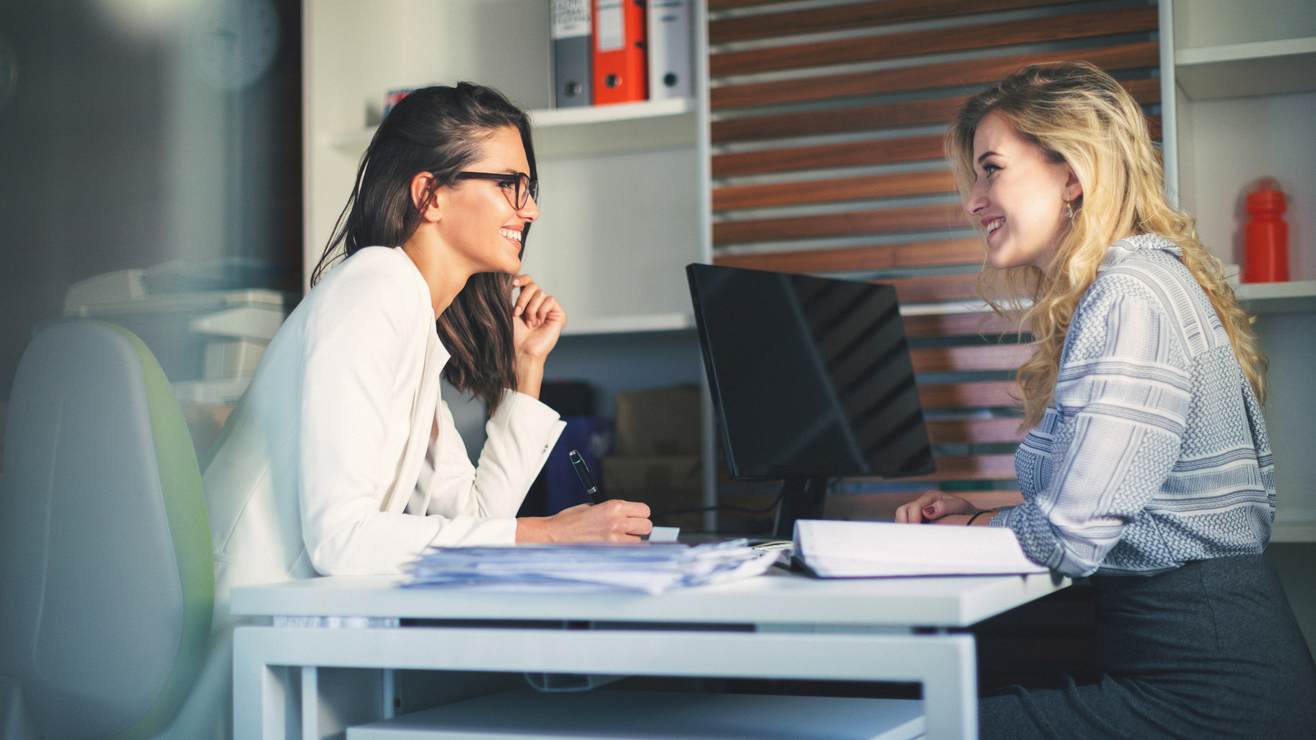 A group of business people are sitting around a table shaking hands.
