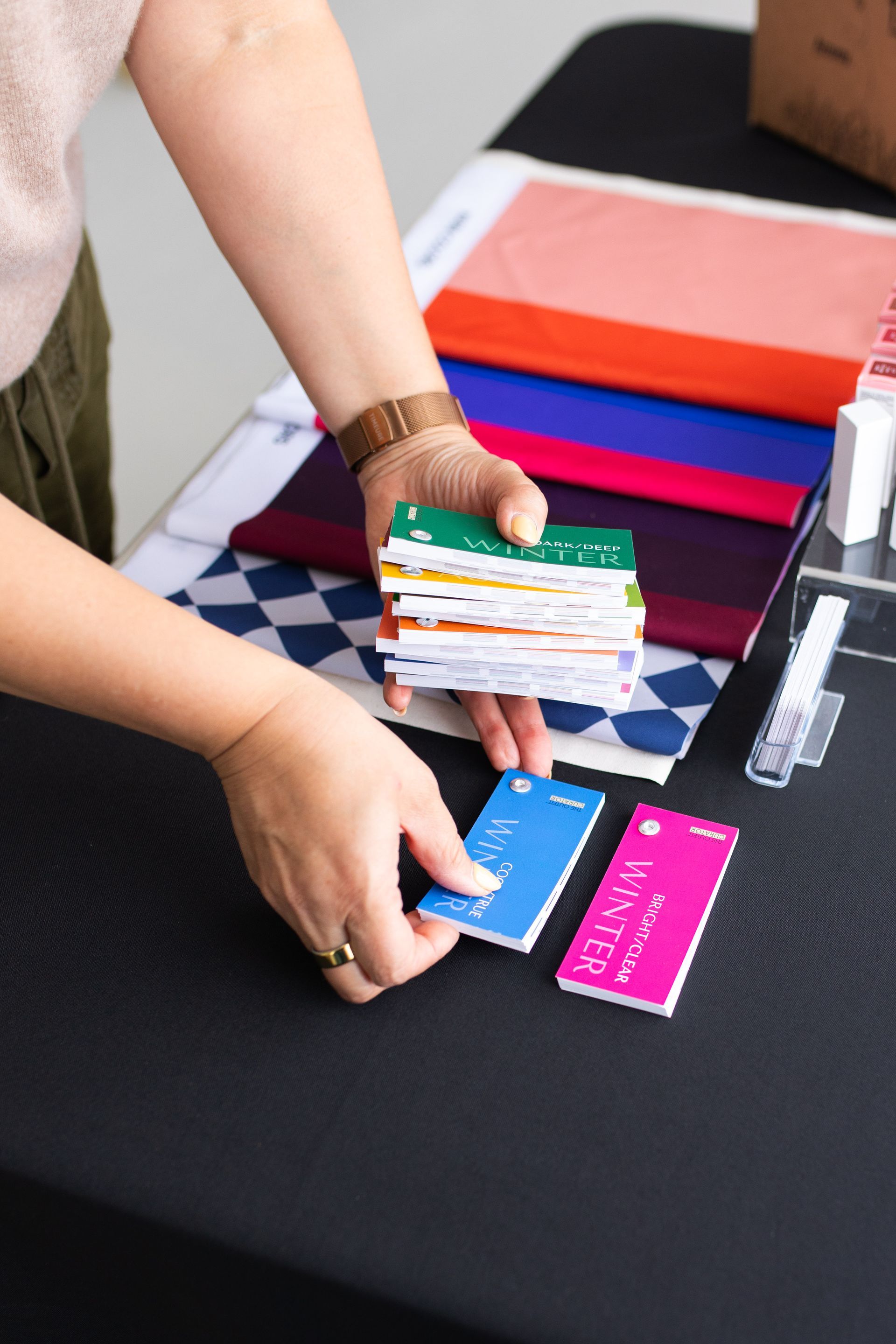 Hands sorting colorful cards on a black table with stacks of fabric swatches.