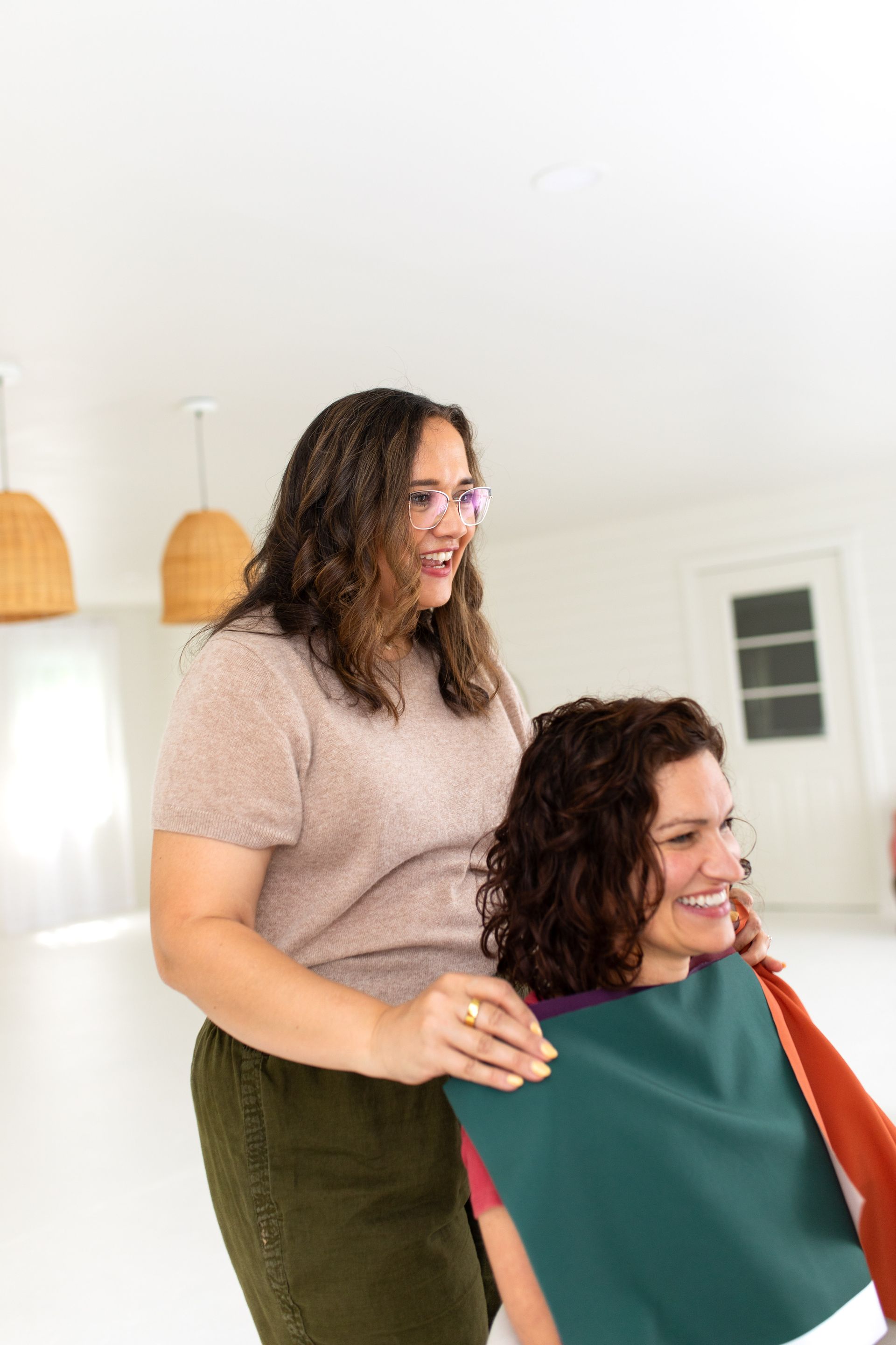 Woman styling a seated client’s hair in a bright salon, both smiling