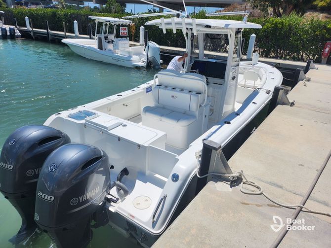 White boat with two outboard motors docked at a pier. Another boat is visible in the background.