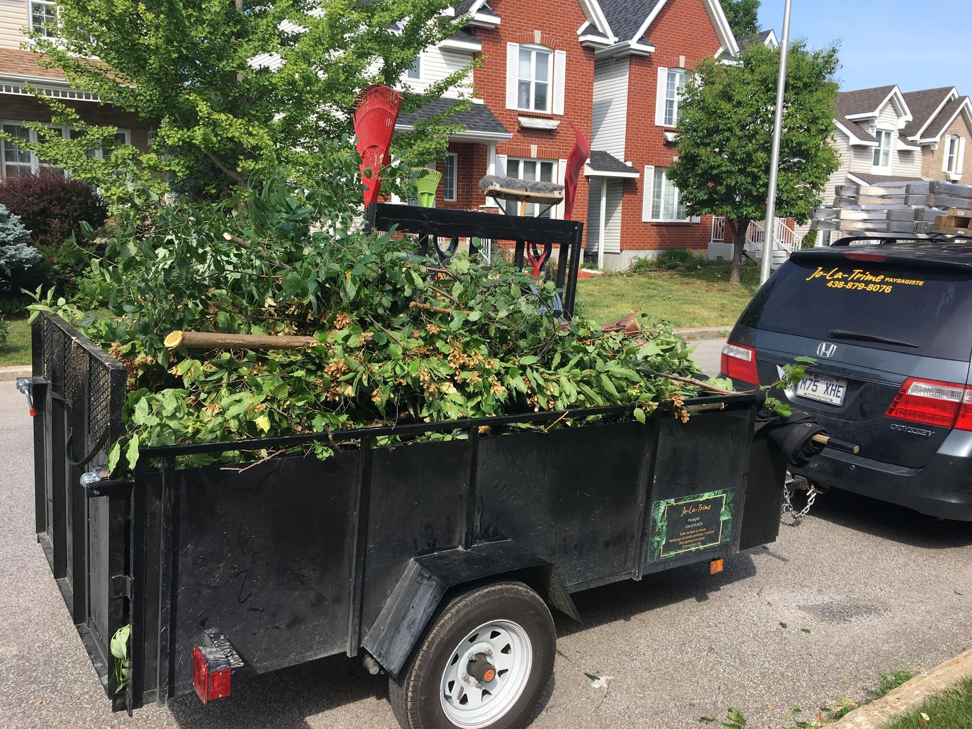 Une remorque remplie de feuilles est garée à côté d'une voiture.