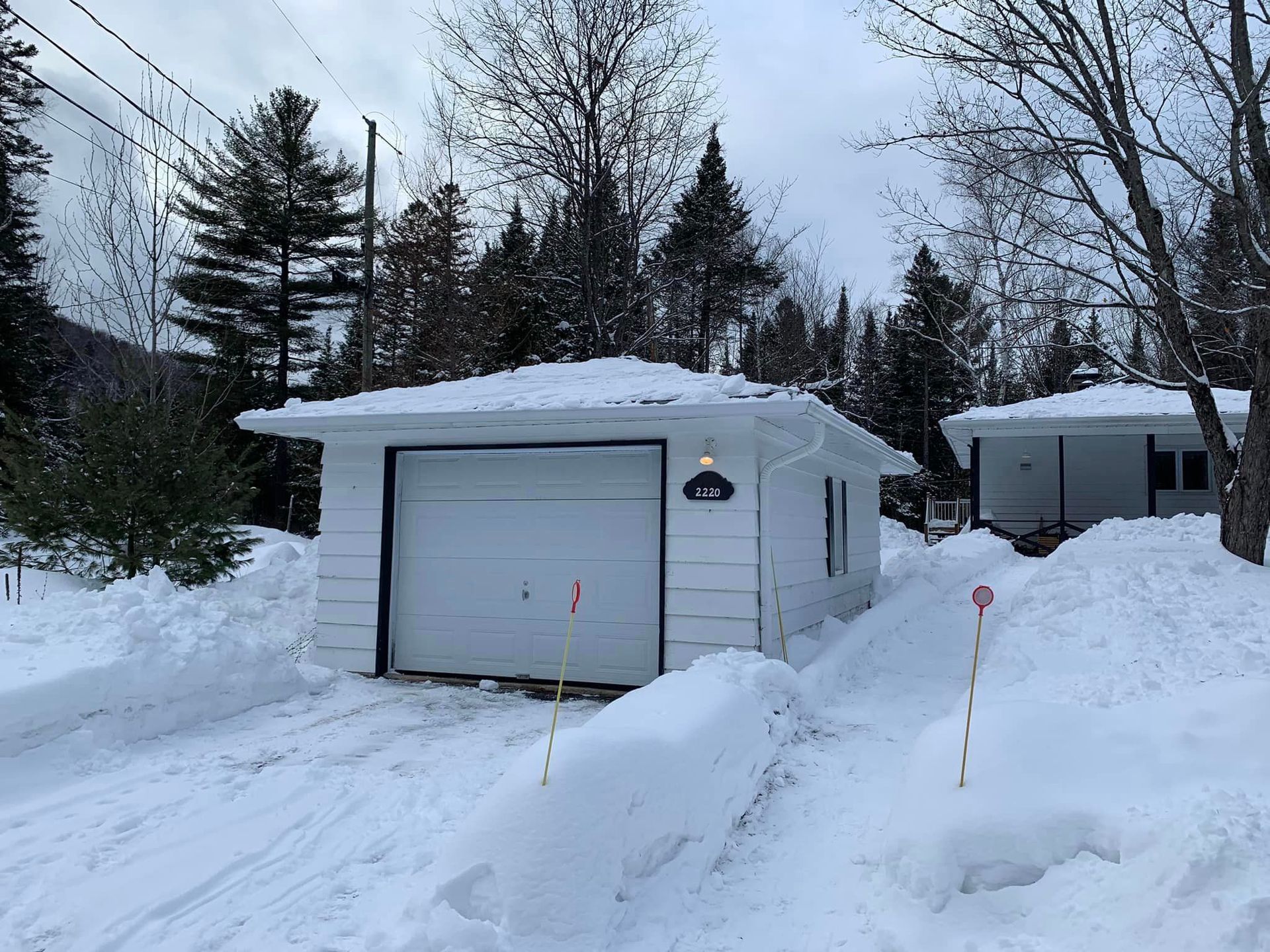 Un garage blanc est entouré de neige et d'arbres.