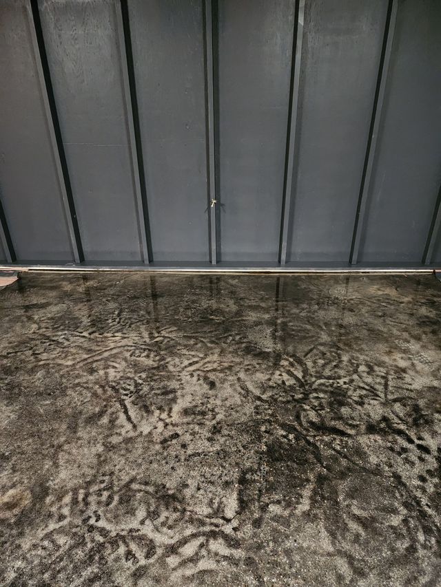 Shiny, grey epoxy floor reflecting light from windows and door, indoors. Green tape at baseboards.