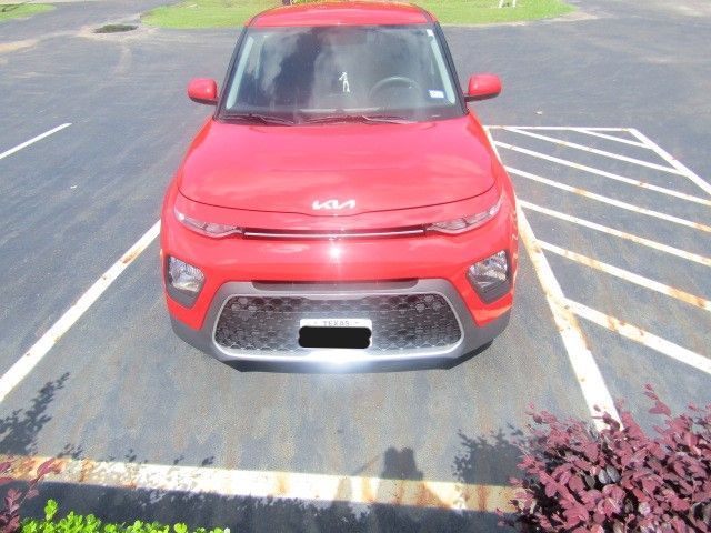 Red Kia parked in a parking lot, front view with white-striped spaces nearby.
