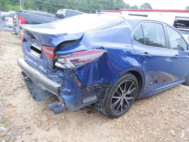Blue sedan with severe rear-end damage in a gravel lot, bumper and trunk crushed after a crash