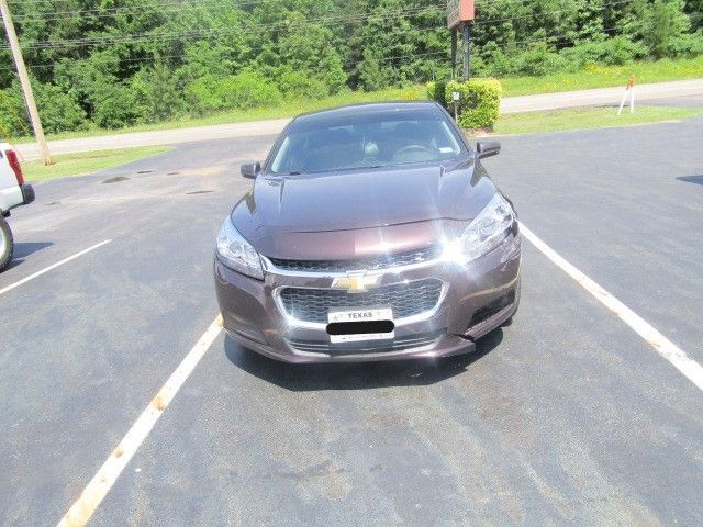 Gray sedan parked in a nearly empty lot, front view, with trees in the background